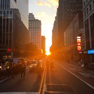 Vehicles on road along buildings at sunset