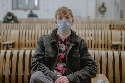 A young man sits at the station waiting for his train, with a mask on his face, curly hair, movement
