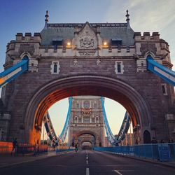 Rear view of cyclist riding bicycle on tower bridge against sky at morning