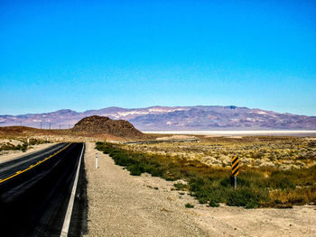 Road leading towards mountains against clear blue sky