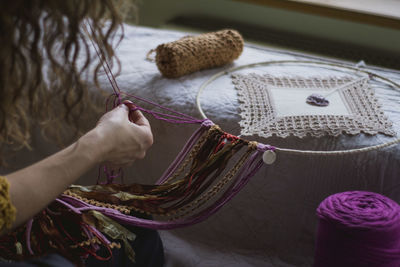 Back view of crop woman creating handmade dreamcatcher with long threads spending time in house