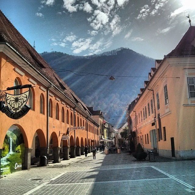 architecture, built structure, building exterior, the way forward, sky, street, diminishing perspective, house, in a row, empty, residential structure, town, residential building, cobblestone, road, transportation, sunlight, mountain, cloud - sky, incidental people