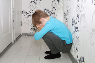 Side view of boy standing against wall at home