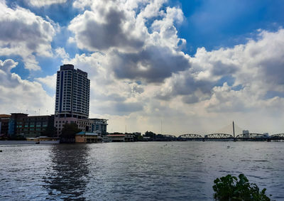 Bridge over river by buildings in city against sky