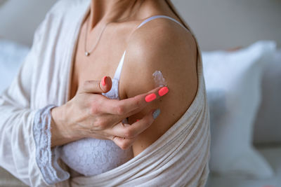 Close-up woman wrapped in robe applying body cream to shoulder after shower
