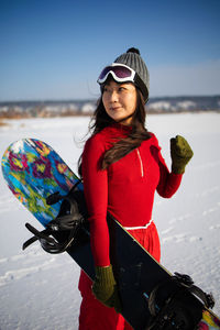 Asian female snowboarder holding snowboard standing on mountain.