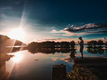 Silhouette man standing by lake against sky during sunset