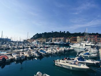 Boats moored at harbor against blue sky