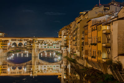 Ponte vecchio over arno river against sky in city at night