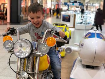 Smiling boy riding toy motorcycle in mall