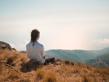 Rear view of man sitting on landscape against mountain