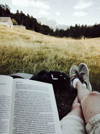 Low section of man reading book on field