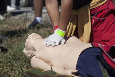 Low section of man practicing cpr on dummy at field during sunny day