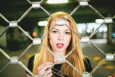 Portrait of beautiful young woman seen through chainlink fence in basement