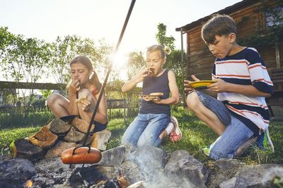Friends eating food by bonfire against plants
