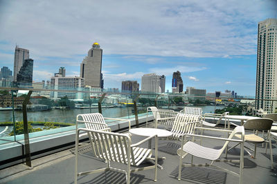 Empty chairs and tables against modern buildings in city against sky