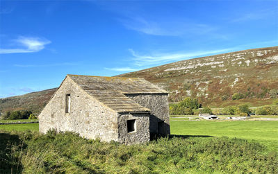 Old barn, with a slate roof, and cattle below the fells in the distance near, arncliffe, skipton, uk