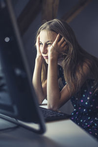 Thoughtful girl using computer while sitting on table