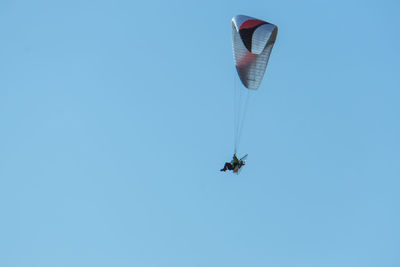 Low angle view of man powered paragliding in clear blue sky