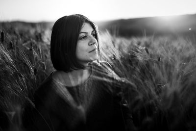 Thoughtful young woman by wheat on farm during sunny day