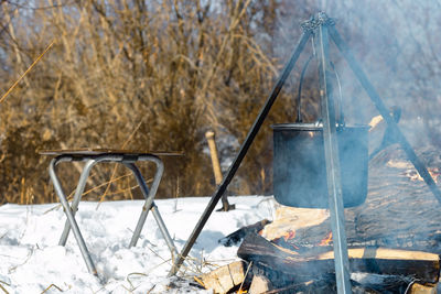 Caked pot in soot over campfire on tripod, winter outdoor cooking at campsite, camping mood