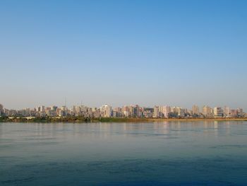 Scenic view of sea by city against clear blue sky