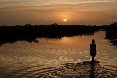 Silhouette person standing in lake against sky during sunset