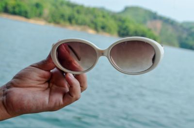 Close-up of hand holding sunglasses against water