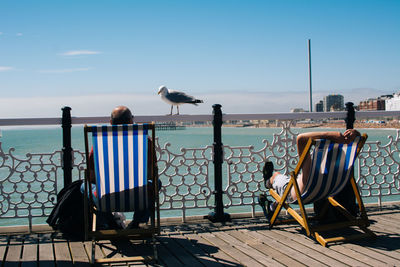 Seagulls sitting on chair by sea against sky