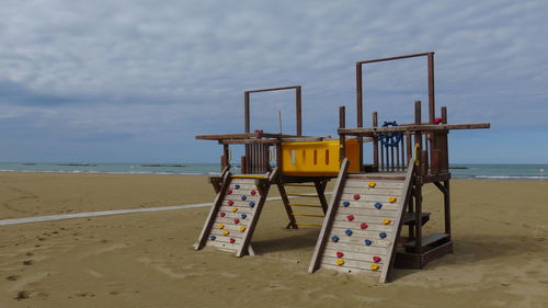 View of playground equipment on beach against cloudy sky