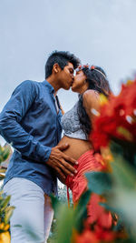 Low angle view of expectant couple kissing while standing against sky