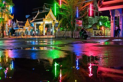 Puddle on street by illuminated temple at night