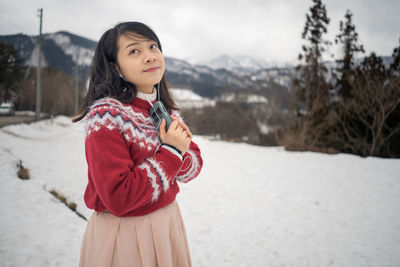 Young woman listening music on mobile phone while standing in snow