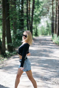 Full length of woman wearing sunglasses on road in forest