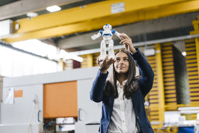 Young woman working in distribution warehouse, looking at toy robot