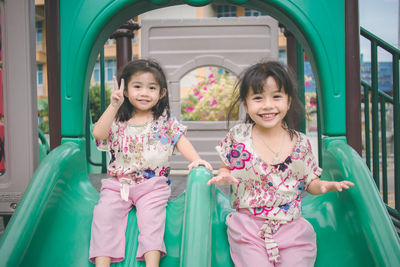 Portrait of cute smiling sisters sliding in park