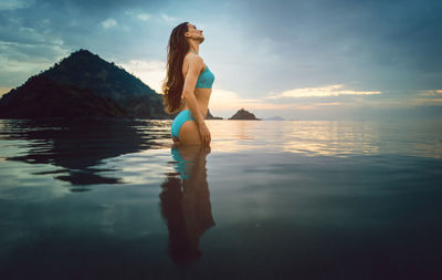 Woman wearing bikini standing in sea against sky