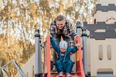 A boy, person with down syndrome walks in the park with his mother, going down the children's slide