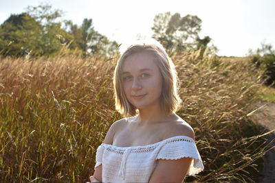 Portrait of smiling young woman standing against plants on field