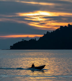 Silhouette boat sailing in sea against cloudy sky during sunset