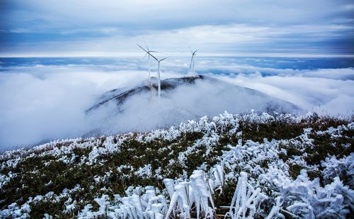 Windmills on mountain over clouds during winter