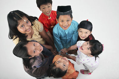 Cute children wearing traditional clothing huddling against white background