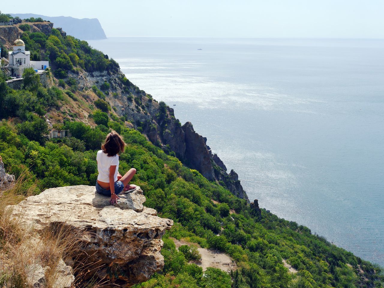 WOMAN SITTING ON CLIFF BY SEA AGAINST SKY