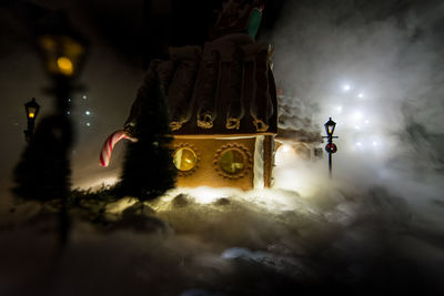 Low angle view of illuminated lighting equipment at gingerbread village with fog from dry ice