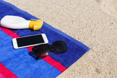 High angle view of mobile phone with sunglasses and spray bottle on towel