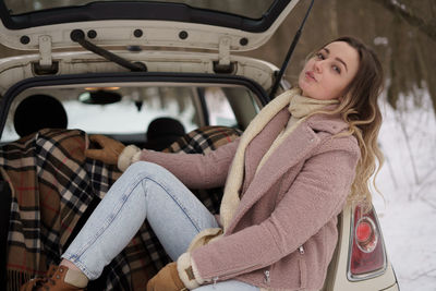 Young woman sitting in car trunk