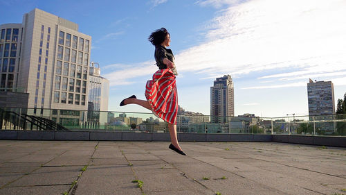 Happy woman wearing striped skirt and jacket on footpath in city