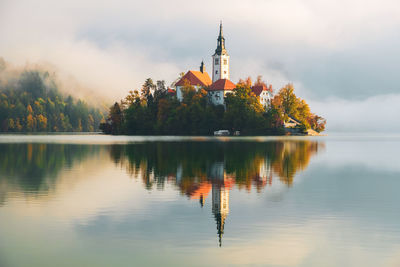 Traditional building by lake against sky during sunset