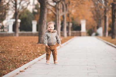 Cute baby girl 1-2 year old wearig casual stylish cloth in autumn park with fall leaves outdoor.