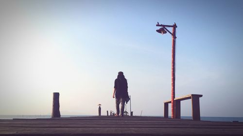 Rear view of woman walking on pier against sky